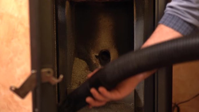 男子使用真空吸尘器清除颗粒炉中的垃圾，在家中清洁颗粒炉内部。用于供暖房屋，电力和能源概念的替代和经济