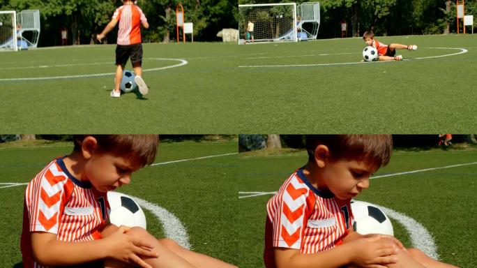 跟踪一个小男孩踢足球的摄像机，在足球场上摔倒和哭泣，4k慢动作