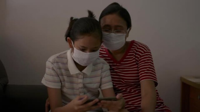 为了防止新型冠状病毒肺炎大流行，母亲和女儿戴着防护口罩一起坐在家里检疫。