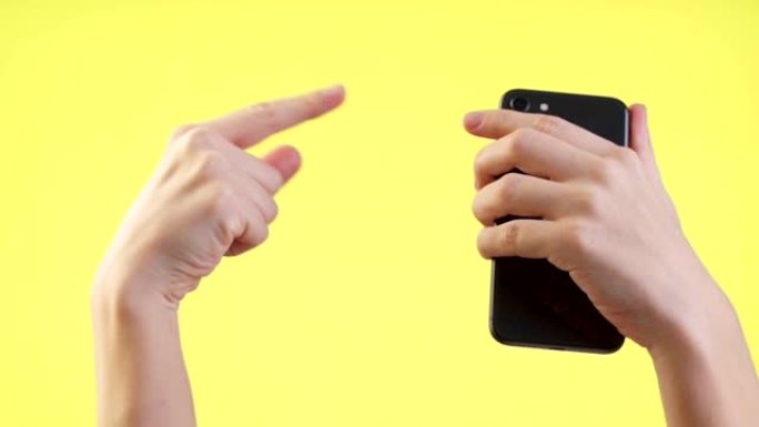 男子手持手机，使用手机，在工作室的黄色背景上显示拳头赢大拇指