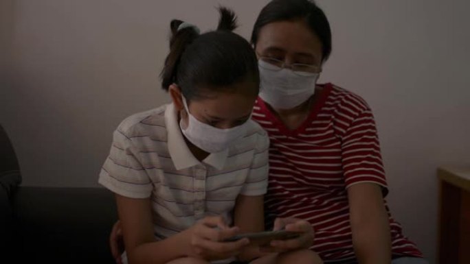 为了防止新型冠状病毒肺炎大流行，母亲和女儿戴着防护口罩一起坐在家里检疫。