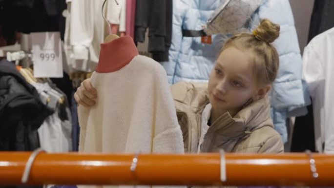 购物时服装陈列室里的年轻少女看夹克。年轻女子在时尚精品店挑选衣服。少女在服装店购物。