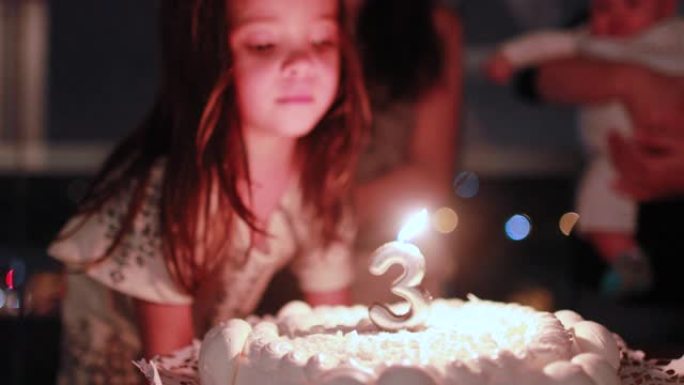 小女孩在庆祝三岁的生日蛋糕上吹蜡烛
