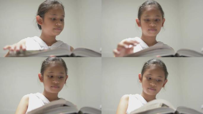 穿着白衬衫的可爱微笑的年轻女孩在图书馆看书。漂亮的女少年喜欢从书中搜索有用的信息和知识。