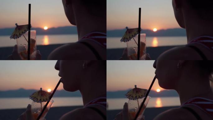 女孩用吸管喝着新鲜的莫吉托，向远处望去，享受着令人惊叹的海洋日落。年轻少年在海边放松和喝饮料的剪影。