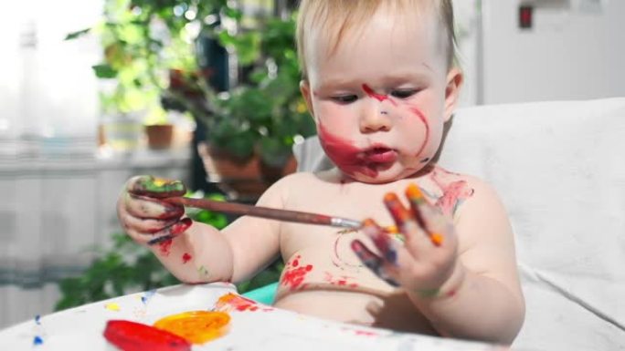 婴儿在家画画。婴儿的肖像婴儿热情地用刷子和油漆画画，并在家里给自己上色