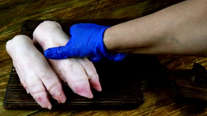 戴着橡胶手套的人的手整齐地将生猪腿放在木制厨房板上。
