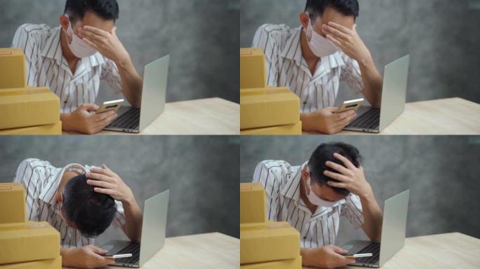 年轻的亚洲失业男子戴着口罩，在销售和包装产品时在网上找工作后感到紧张和担忧