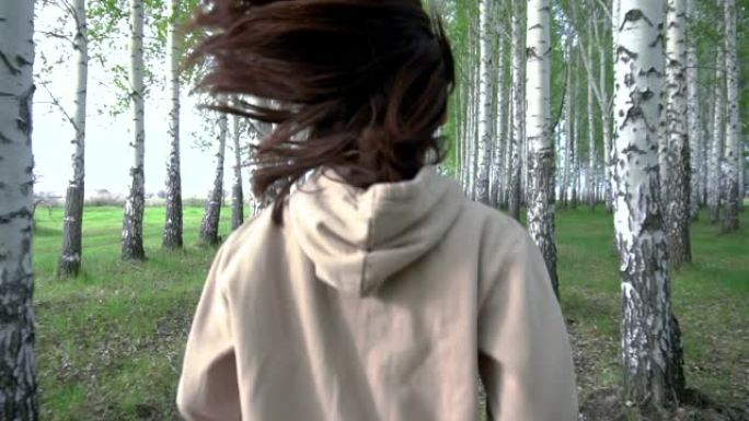 一名年轻女子以慢动作穿过白桦林。这个女孩在树丛之间奔跑。后视图。