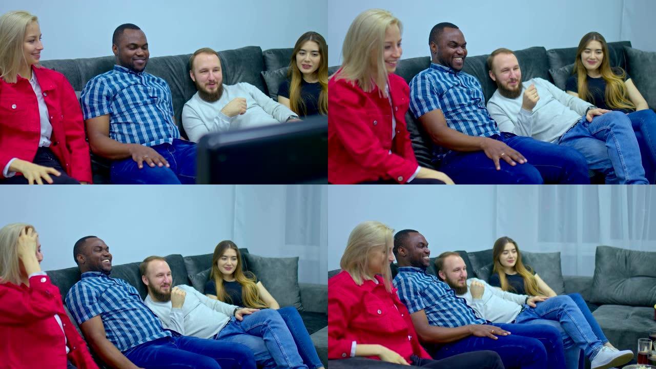 由不同国籍的人组成的团队坐在沙发上看电视。黑皮肤的家伙在公司休息。