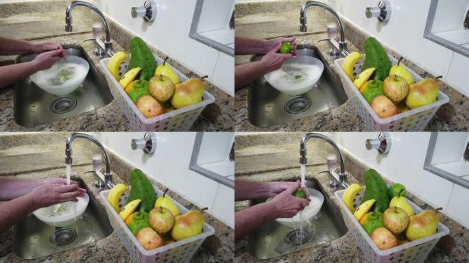 双手特写，在家用厨房水槽中清洗水果 (柠檬)