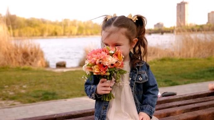 小女孩坐在公园的长椅上，摆着一束鲜花，她嗅着鲜花。