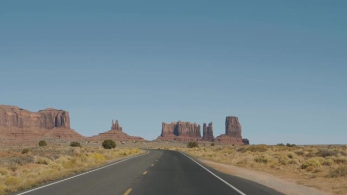 驾驶在著名的道路在纪念碑谷美国红岩丘陵的背景