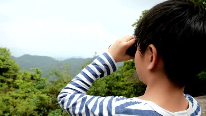 小男孩在山顶上用望远镜看风景