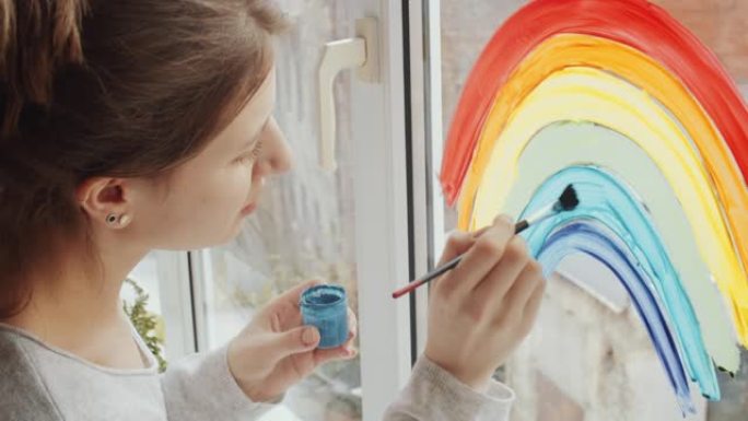 女人用油漆和刷子在窗户玻璃上画彩虹