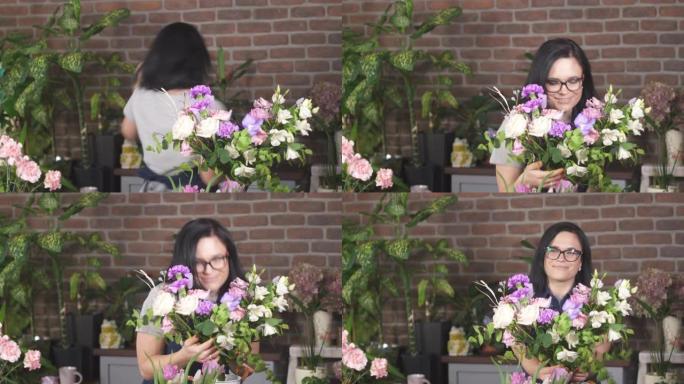 戴眼镜的黑发女孩笑着跳舞，吸入一束鲜花。女性微笑着享受情人节捐赠的鲜花。女人小企业主在成功中快乐。