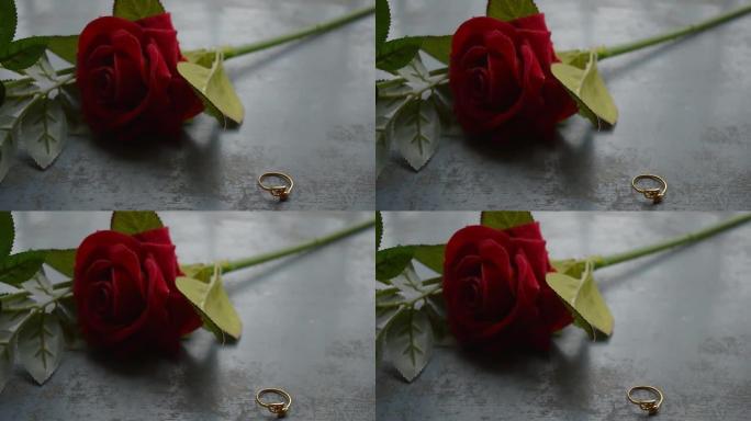 在乡村金属地板上关闭黄金订婚戒指珠宝。背景中柔和的浪漫红玫瑰花朵。情人节婚礼和假期的爱情提议或提议概