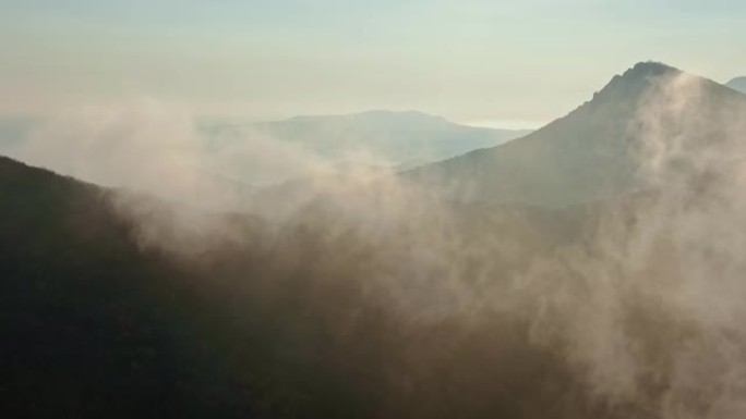 空中勘测在秋天的日落中飞越山峦丛生的森林和雾气覆盖的山坡