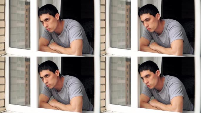 一个悲伤的家伙站在窗前。隔离和检疫期间的抑郁和问题。