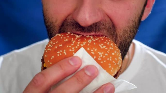 特写，一个有茬的男人在吃汉堡。用一只手拿着芝士汉堡。它不会导致健康的生活方式，损害健康和新陈代谢。错
