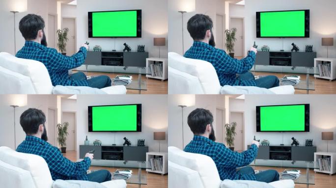 留着胡子的男人坐在客厅的沙发上，在绿屏上看电视切换频道改变音量