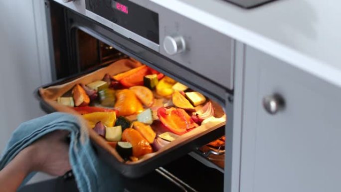 女人烤盘蔬菜在烤箱里吃素食