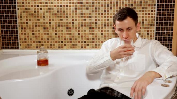 穿着裤子和衬衫的醉酒男子躺在浴缸里喝酒