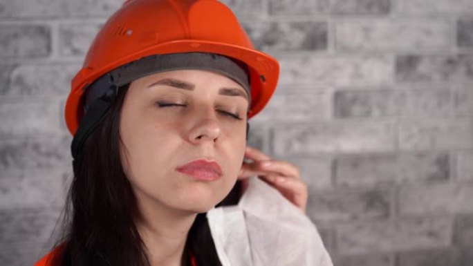 灰色砖墙背景下工作服去除医用口罩的女建筑工人