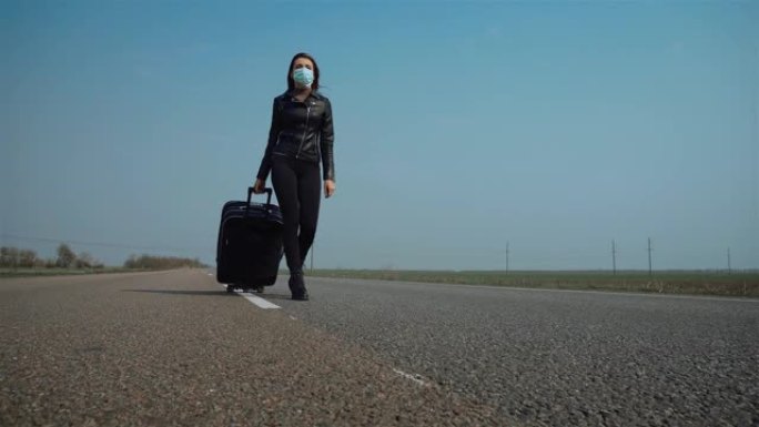 戴着医用口罩的年轻商务女士在柏油路冠状病毒检疫时带着轮子上的手提箱行走