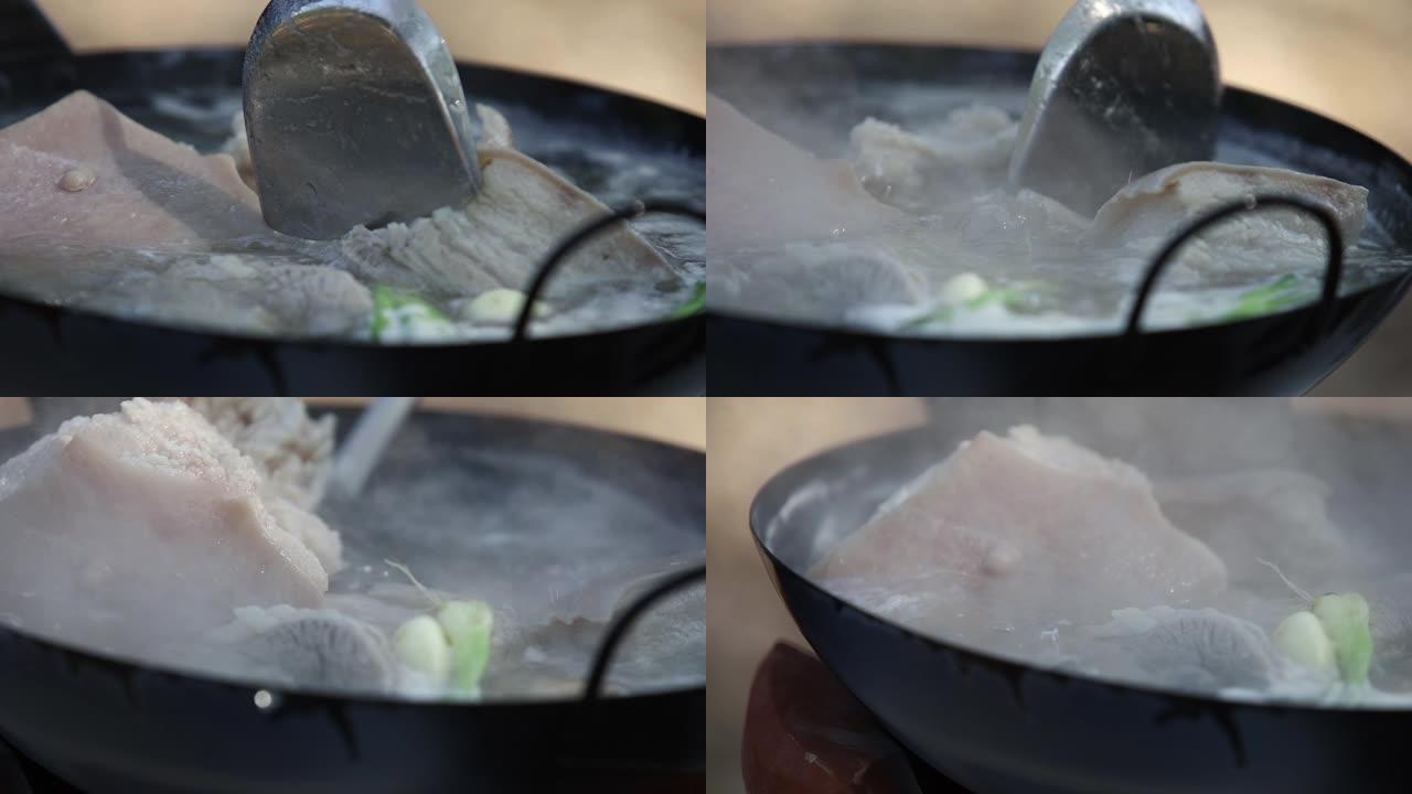 大五花肉正在用蔬菜在黑锅的沸水中烹饪。