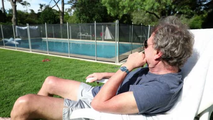 老人坐在外面休息，俯瞰后院的游泳池。享受退休的老年人
