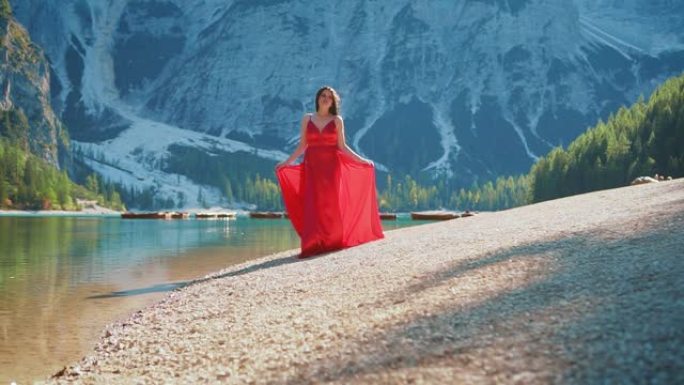 神秘性感的女人走过奢华的红裙。幻想迷人的设计长发丝绸飘飘。慢镜头自然，令人惊叹的风景布雷斯湖，白云石