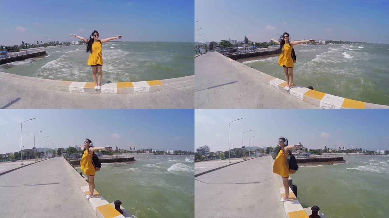 快乐的亚洲女人，用耳机在阳光明媚的日子走在华欣码头，生活方式的概念。