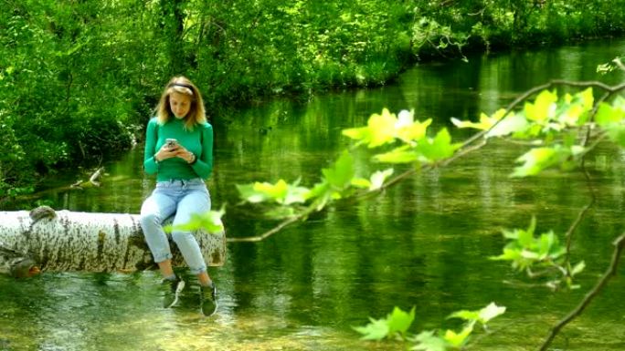 年轻女子在森林灌木丛中的河上带着智能手机