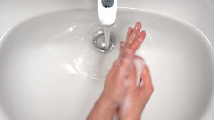 人在浴室水龙头流动的温水下用泡沫肥皂洗手，去除人体皮肤上的脏污和病毒。护肤的日常卫生规则