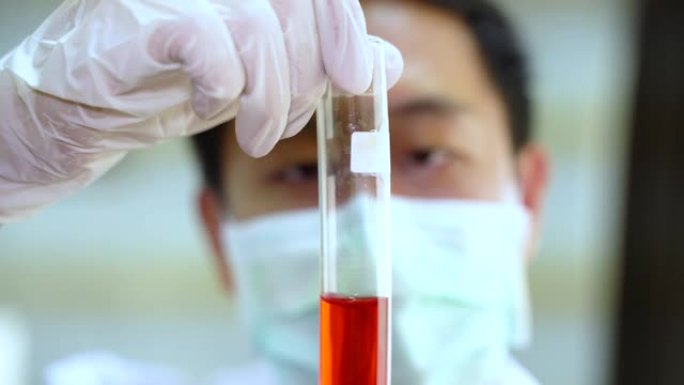 用红色化学溶液拿着实验室烧瓶的白色制服的亚洲男性科学家的特写镜头。化学、科学、生物学、毒理学、研究与