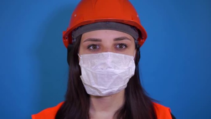 蓝色背景上戴着医用面具的年轻女子的肖像。成年女性用口罩遮住脸，以保护自己免受疾病的侵害。冠状病毒流行