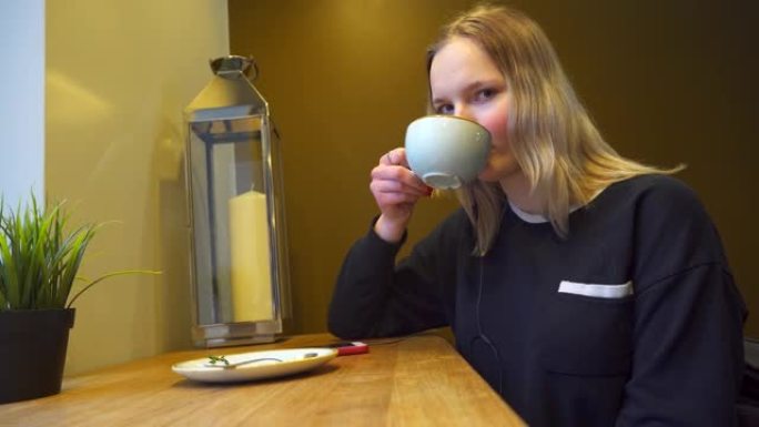 年轻女子少年在咖啡馆喝茶或咖啡，戴着耳机听音乐。