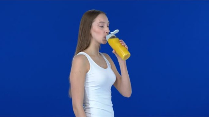 美丽的长发女孩喝运动瓶中的橙汁; 简介。