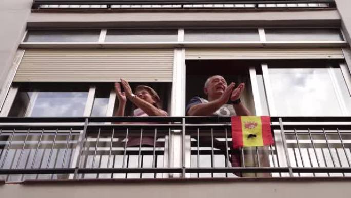 年长的夫妇在窗口鼓掌支持人们反对冠状病毒
