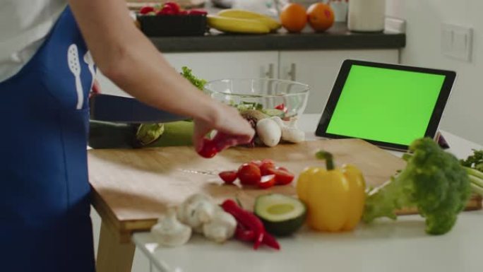 那个女人正在切樱桃番茄，看着平板电脑。绿屏平板电脑。沙拉准备。4K