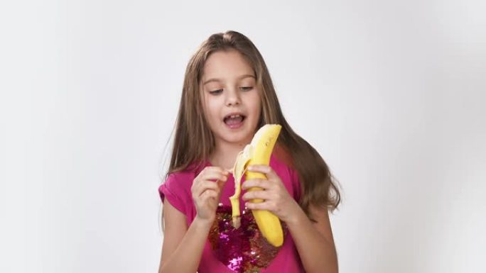 女孩和香蕉跳舞。一个女孩剥香蕉，吃香蕉。一个正在吃香蕉的饥饿女孩的快乐情绪。