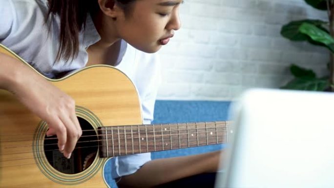 年轻的亚洲妇女练习和学习如何在笔记本电脑显示器上弹吉他。女吉他手在线观看教程