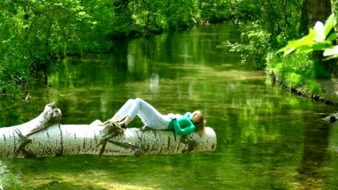 年轻女子躺在森林河上方的原木上