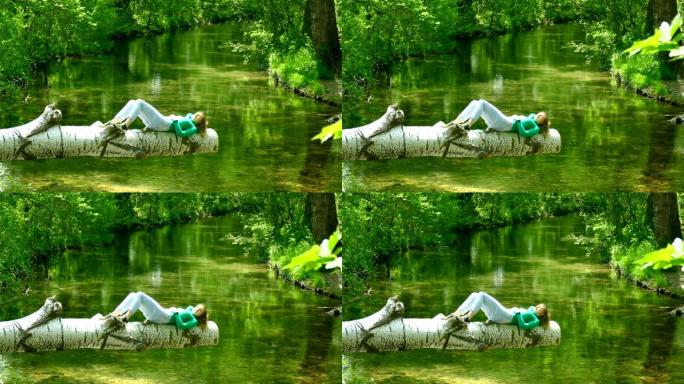 年轻女子躺在森林河上方的原木上