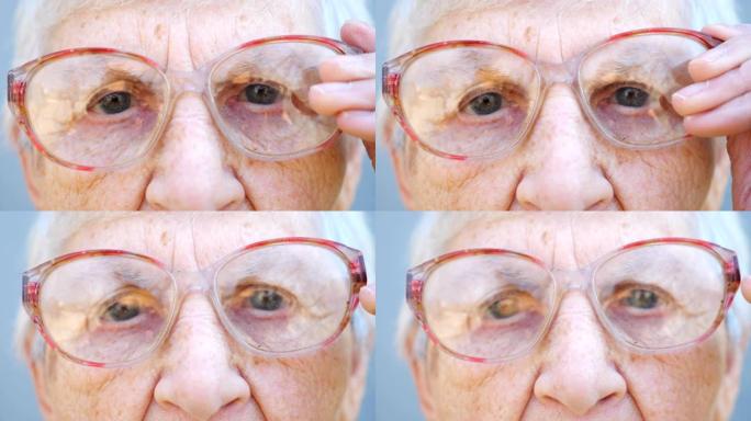 沉思的眼镜中奶奶的细节肖像。关闭女性养老金领取者的皱纹脸，看着相机并调整眼镜。奶奶悲伤的表情。慢动作
