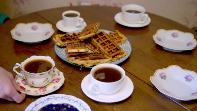 女人把杯子和碟子放在桌子上。有茶和咖啡的晚餐。