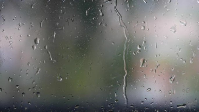 强烈的雨水冲向窗户玻璃并流下来。特写。雨季玻璃背景上的雨滴