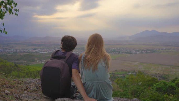 一对年轻的游客坐在山顶上，可以欣赏山谷的壮丽景色