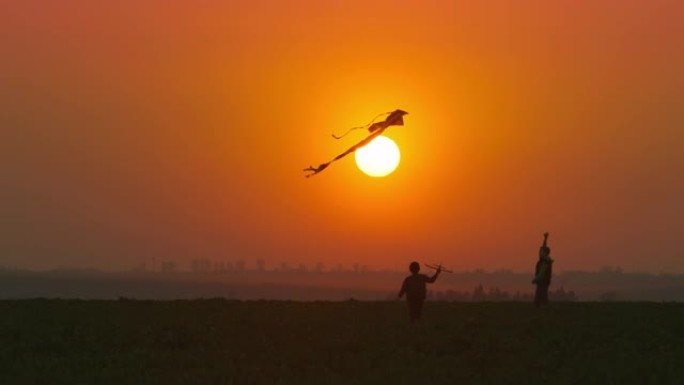 一个手里拿着玩具飞机的小男孩正在跑向正在玩风筝的哥哥。日落时的户外游戏。4k